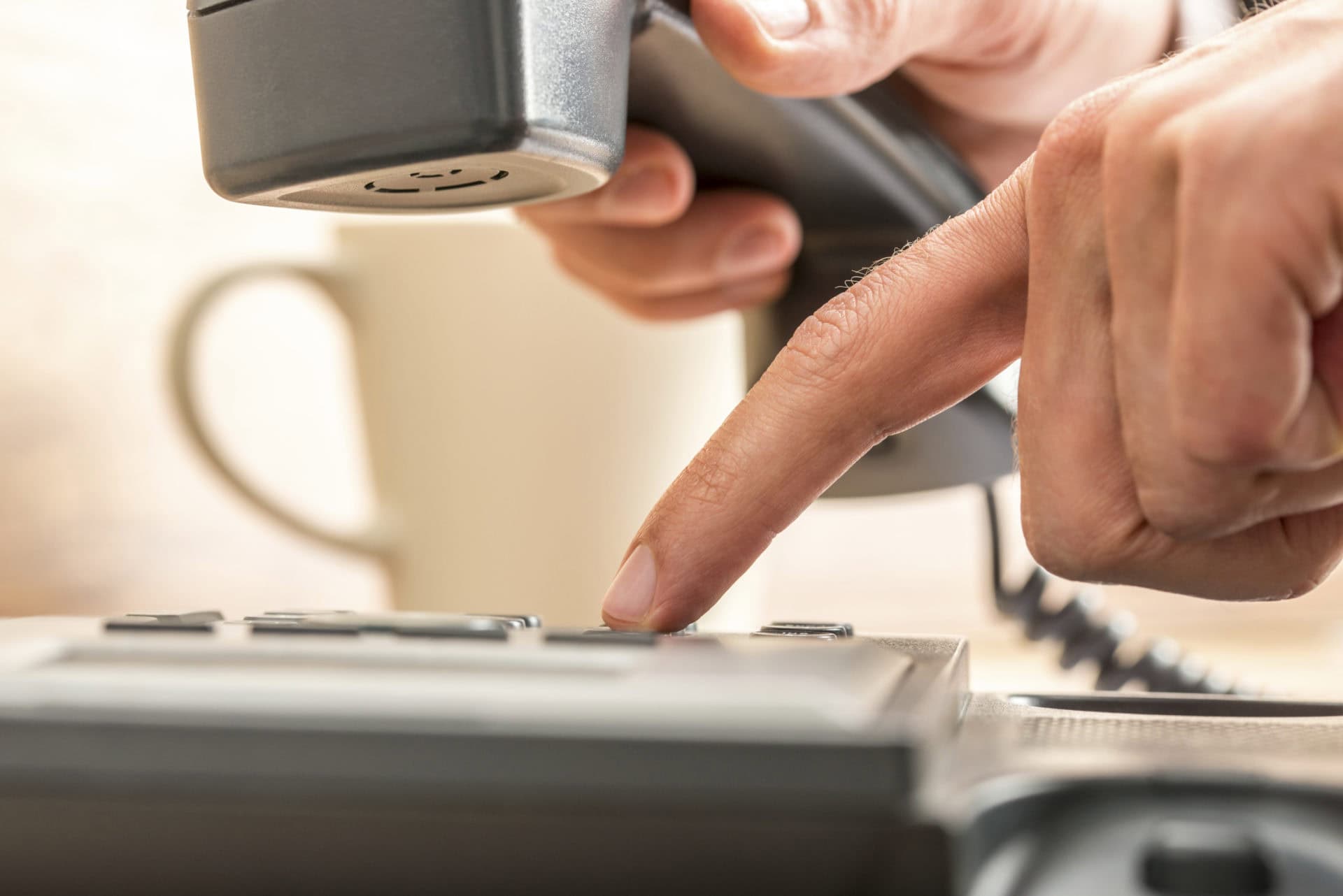 Close up Human Index Finger Dialing on Black Telephone on Top of the Table with a Cup of Coffee on the Side.