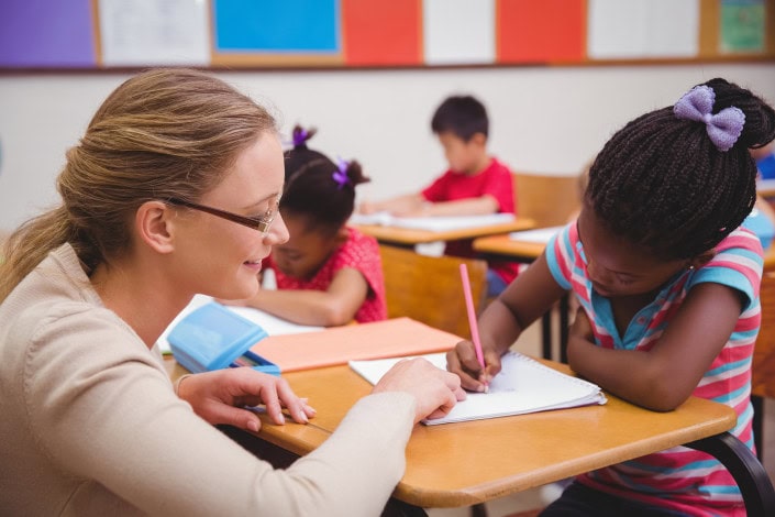 Cute pupil getting help from teacher in classroom at the elementary school